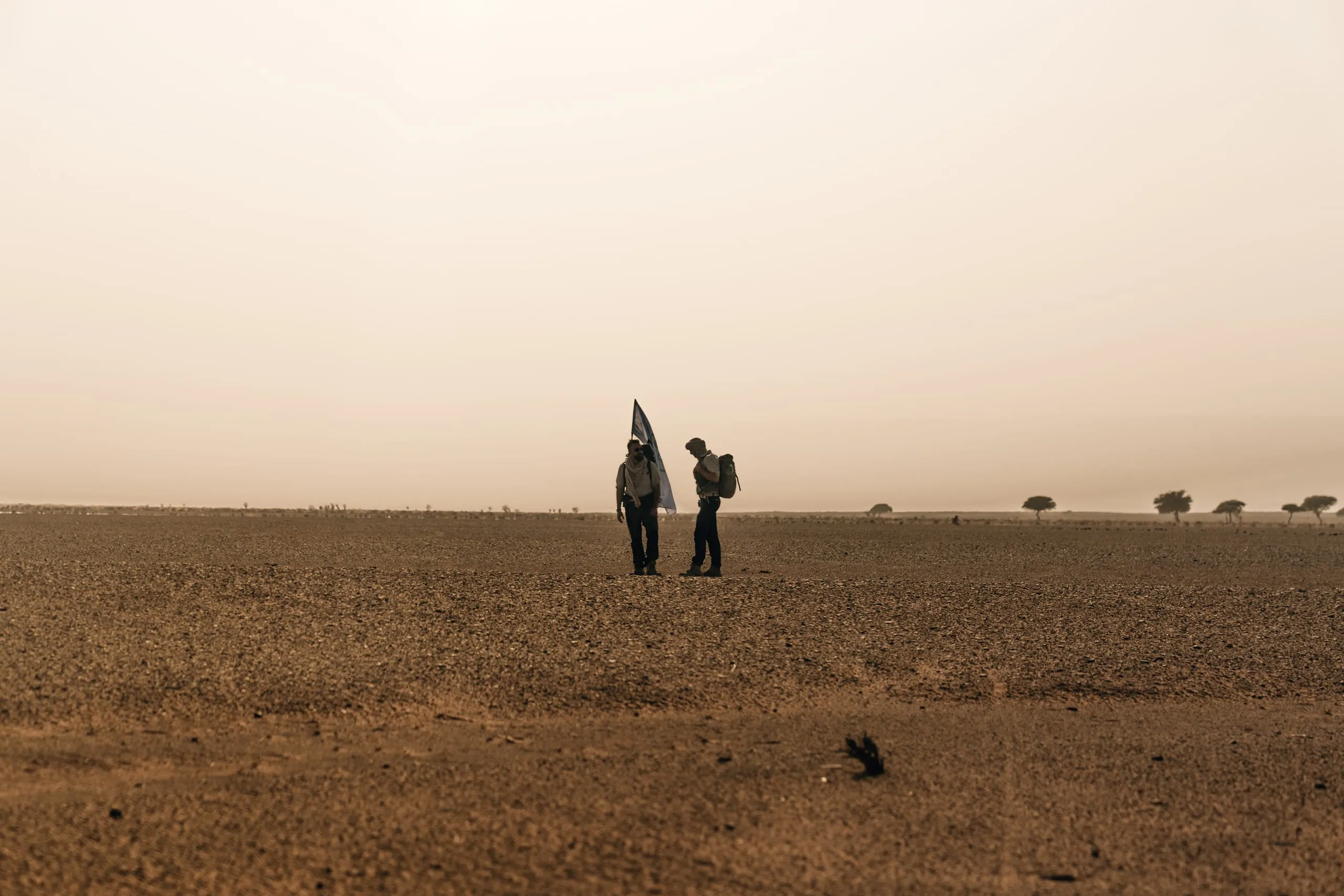 Zwei Personen mit einer Fahne auf einer Geröllebene in der marokkanischen Sahara